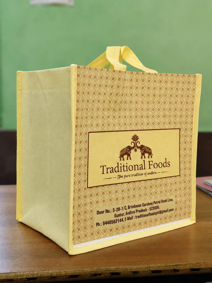 Cream 110 GSM stitched non woven bag with a patterned side patty and loop handles, standing on a table